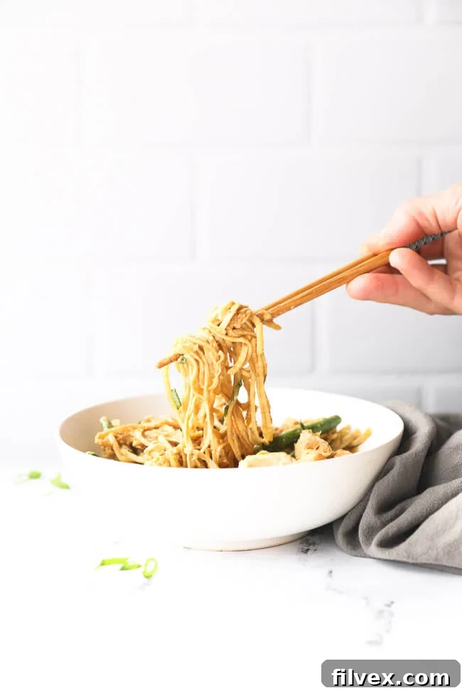 Straight on image of pulling some creamy peanut butter chicken noodles out of a bowl with chopsticks. 