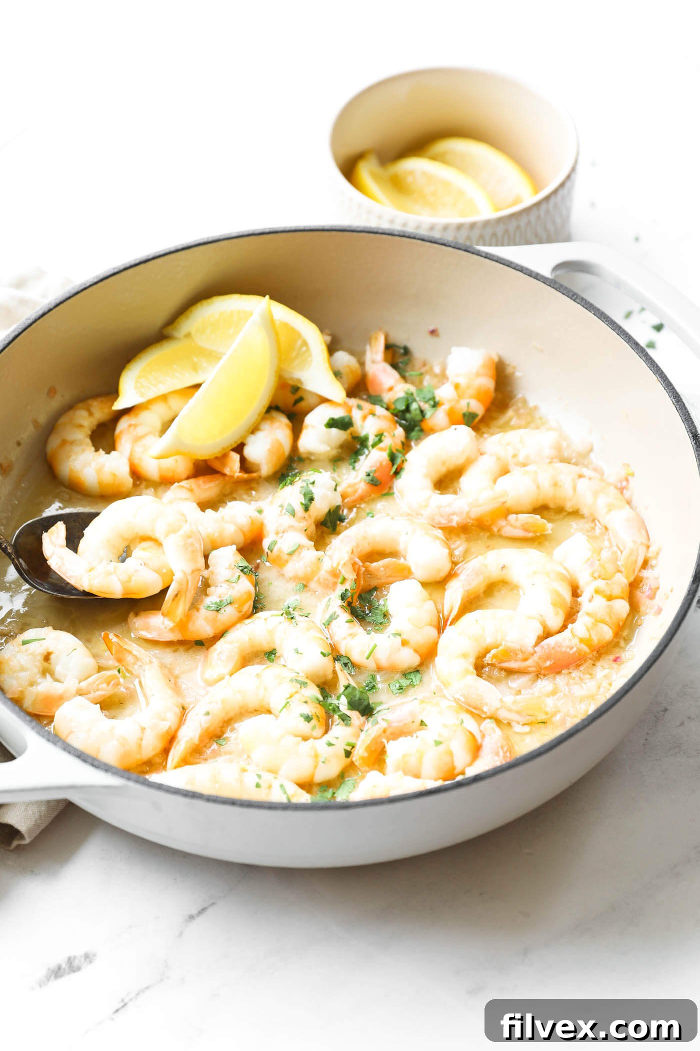 Angled image of garlic butter shrimp in a skillet. Topped with chopped cilantro and lemon wedges.
