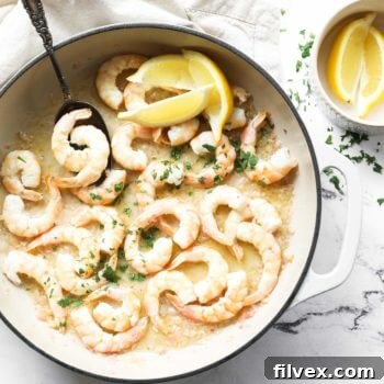 Overhead image of a skillet with garlic butter shrimp. A serving spoon dug in, and topped with chopped cilantro and lemon wedges.