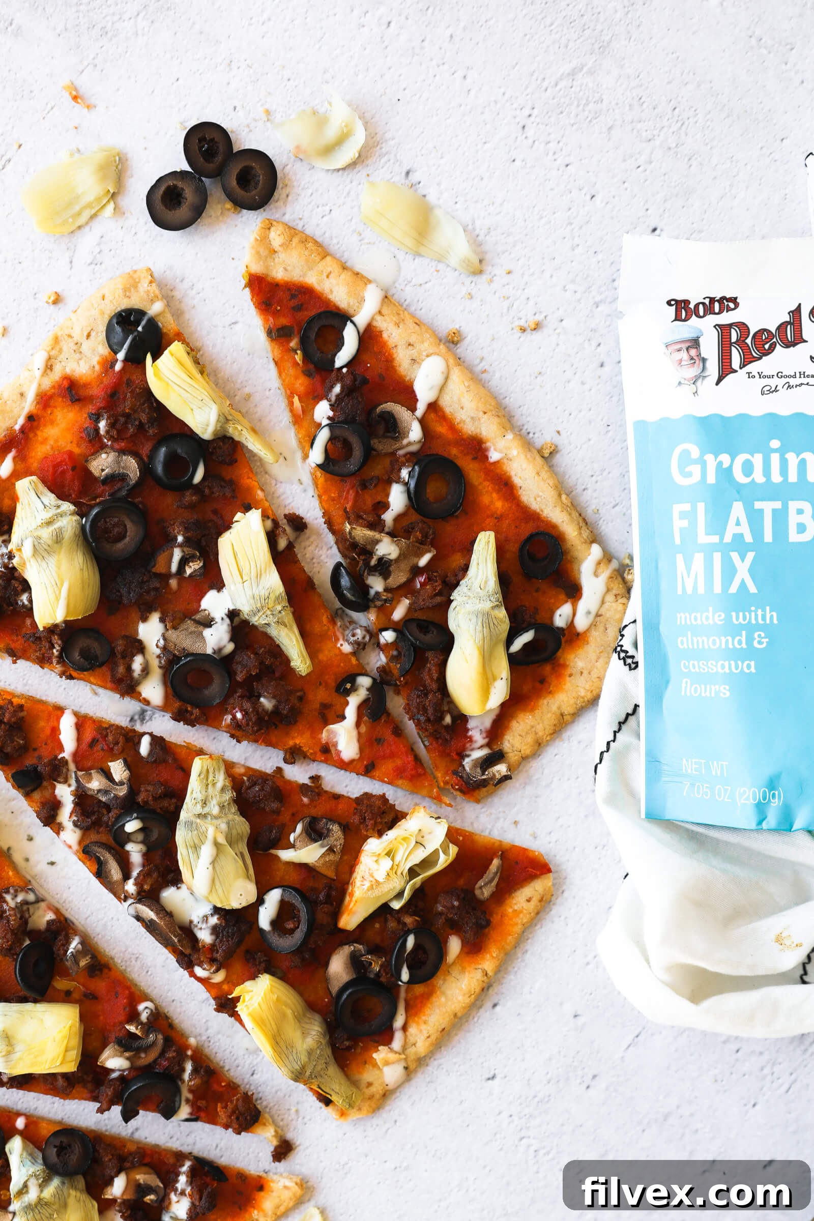 Flatbread pizza slices arranged around a package of Bob's Red Mill Grain Free Flatbread Mix, showcasing the simplicity of ingredients.