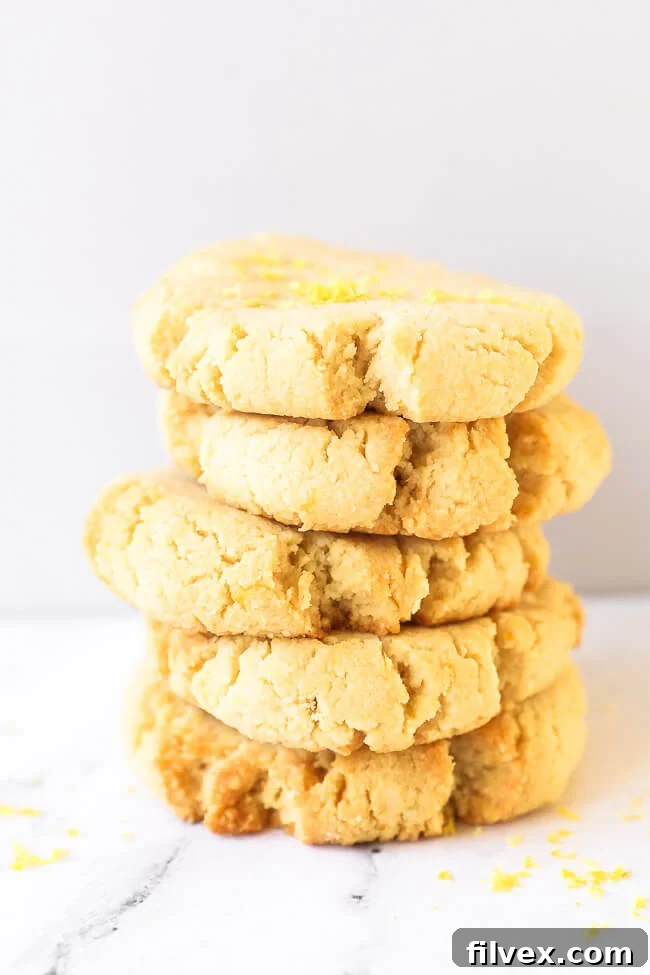 A stack of five gluten free shortbread cookies with lemon zest sprinkled on top. Perfectly baked and stacked gluten-free lemon shortbread cookies, showcasing their golden edges.
