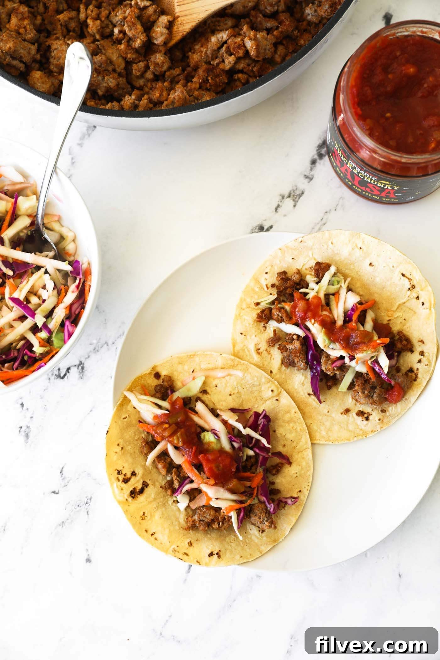 Three perfectly assembled ground pork tacos with vibrant cabbage and avocado slaw, garnished with fresh cilantro and lime wedges, presented in a rustic bowl.