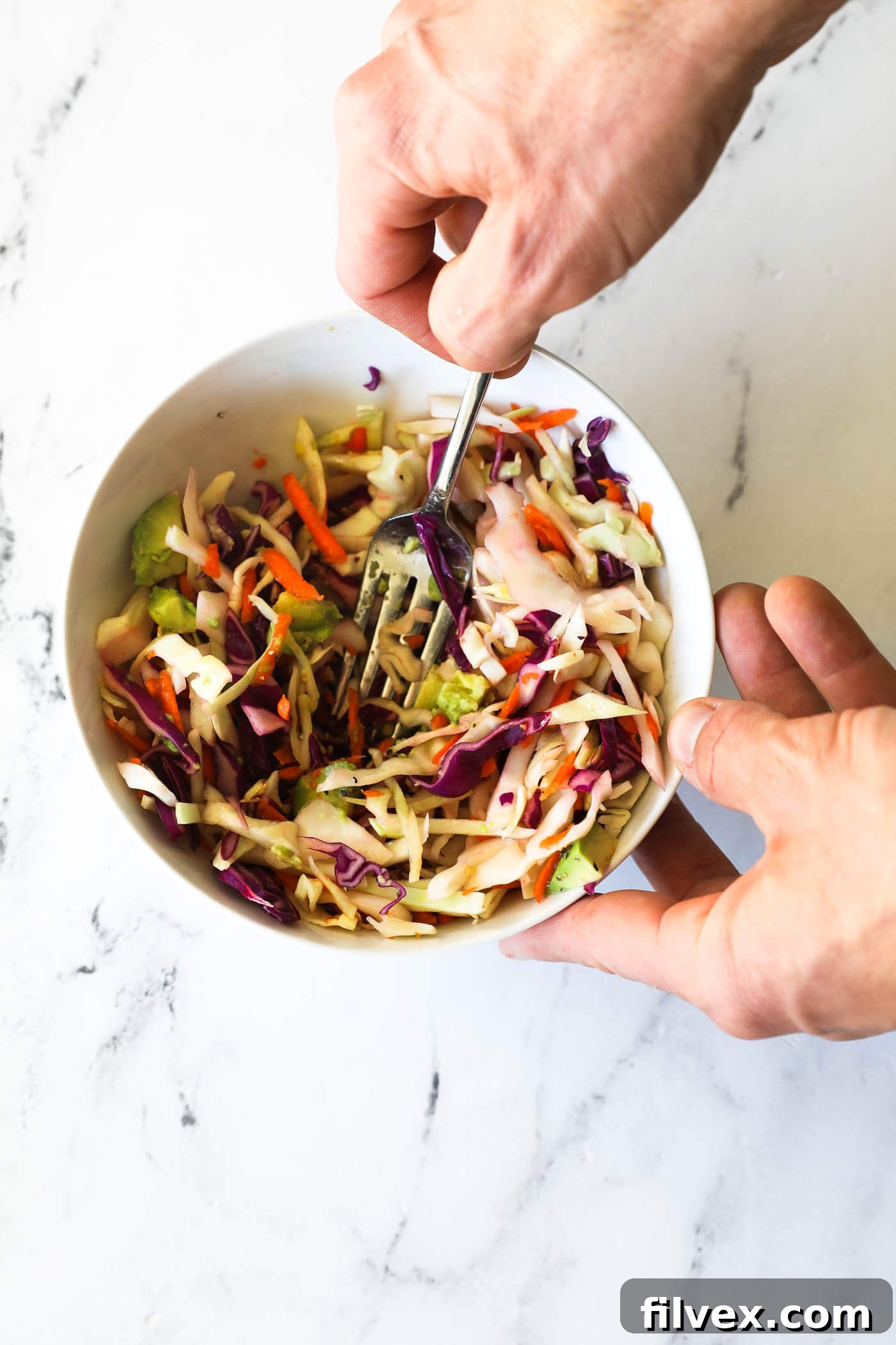 A vibrant bowl of freshly mixed coleslaw featuring shredded cabbage, carrots, and chunks of creamy avocado, dressed with lime juice, ready to be a delicious taco topping.