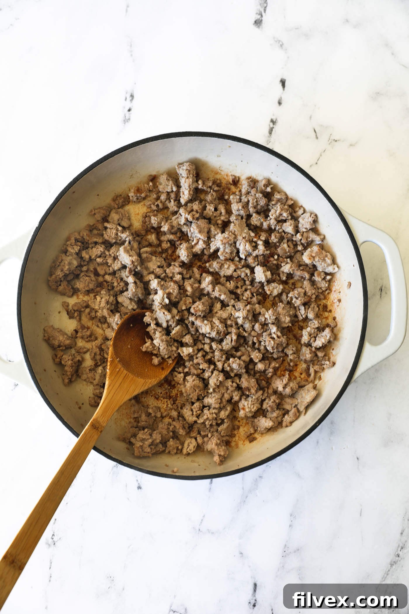 Close-up shot of ground pork browning in a hot non-stick skillet, being expertly broken apart into fine pieces with a wooden spatula, ensuring even cooking and crispy bits.