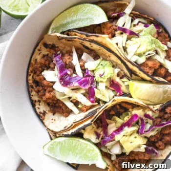 Three ground pork tacos with fresh cabbage and avocado slaw in a bowl, garnished with bright lime wedges – a perfect visual of a healthy and delicious meal.