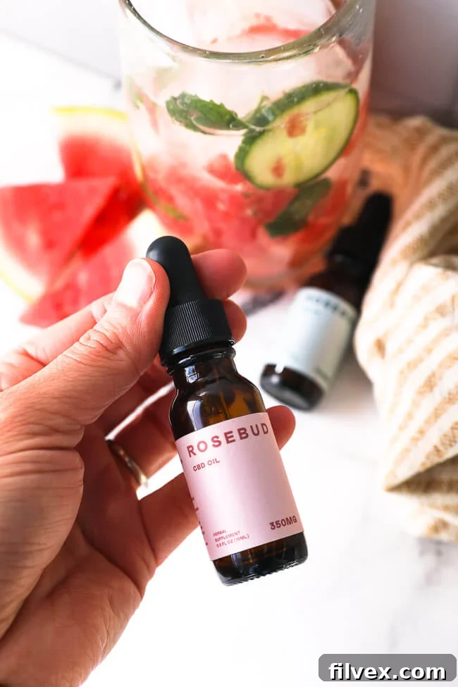 Holding a bottle of CBD oil with watermelon mojito mocktail in the background. 