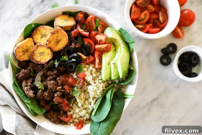 Delicious ground beef taco bowl with vibrant greens, fried plantains, and cauliflower rice, presented horizontally.