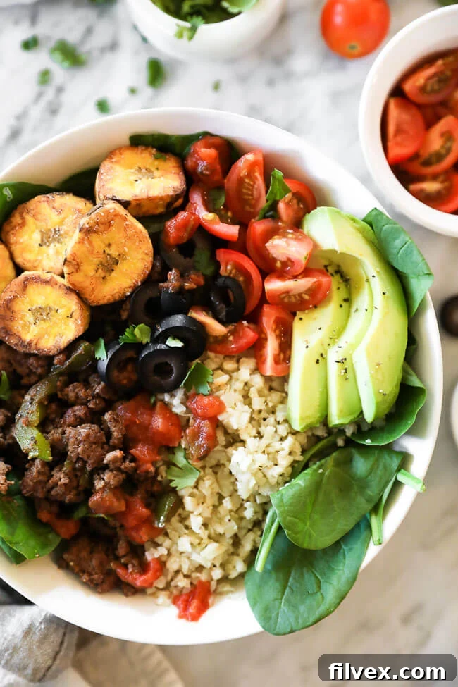 Close-up vertical shot of a vibrant ground beef taco bowl featuring fresh greens, golden plantains, and fluffy cauliflower rice.