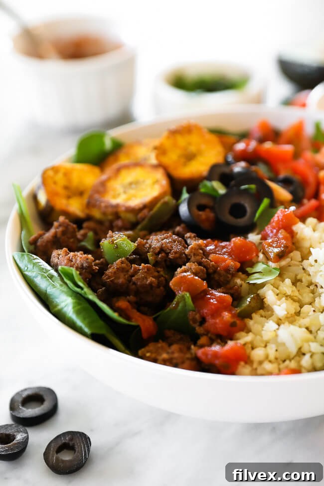 Angled close-up view of a hearty ground beef taco bowl with mixed greens, plantains, and cauliflower rice.