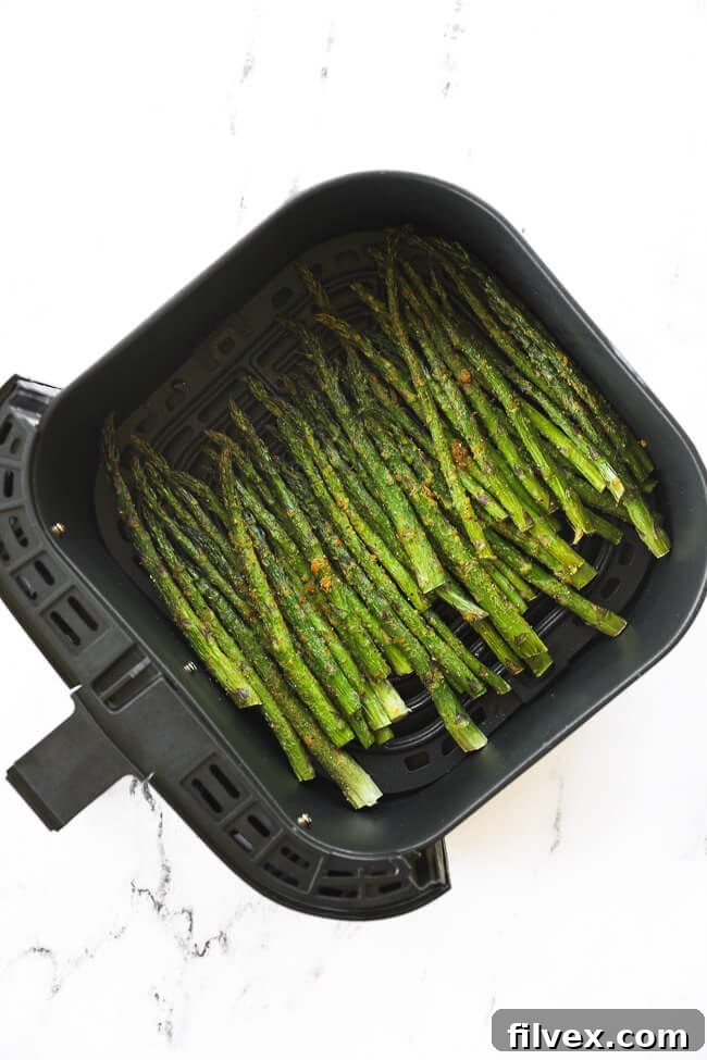 Asparagus after cooking in the air fryer basket, showing its crispy texture.