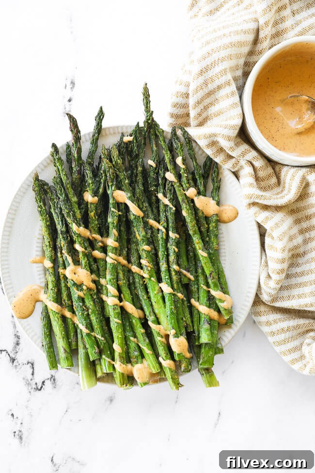 Air fryer asparagus on a plate with chipotle aioli drizzled on top, emphasizing an extra flavor option.