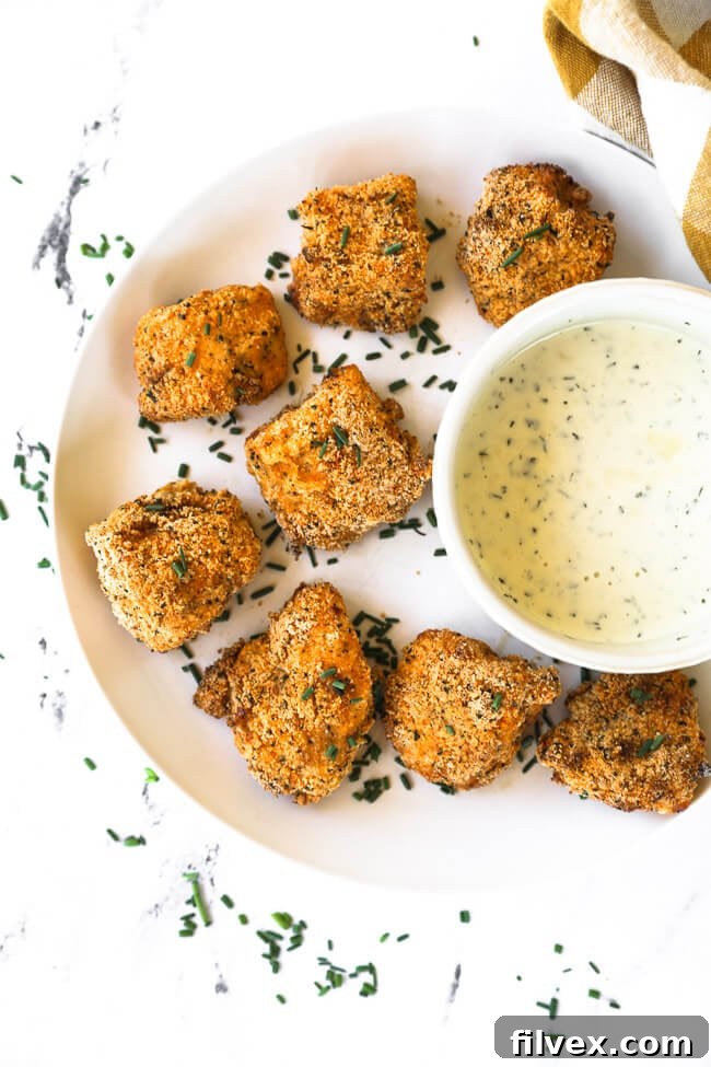 A plate of golden-brown, crispy air fryer chicken nuggets, accompanied by a ramekin of creamy ranch dipping sauce.