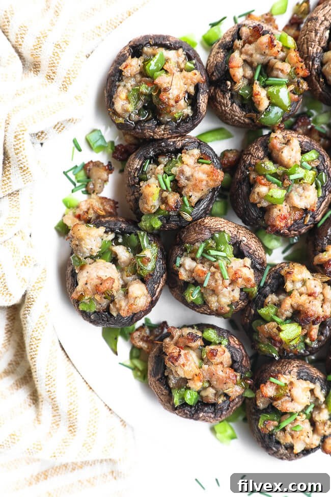 Close-up of baked sausage stuffed mushrooms on a white plate, garnished with fresh herbs.