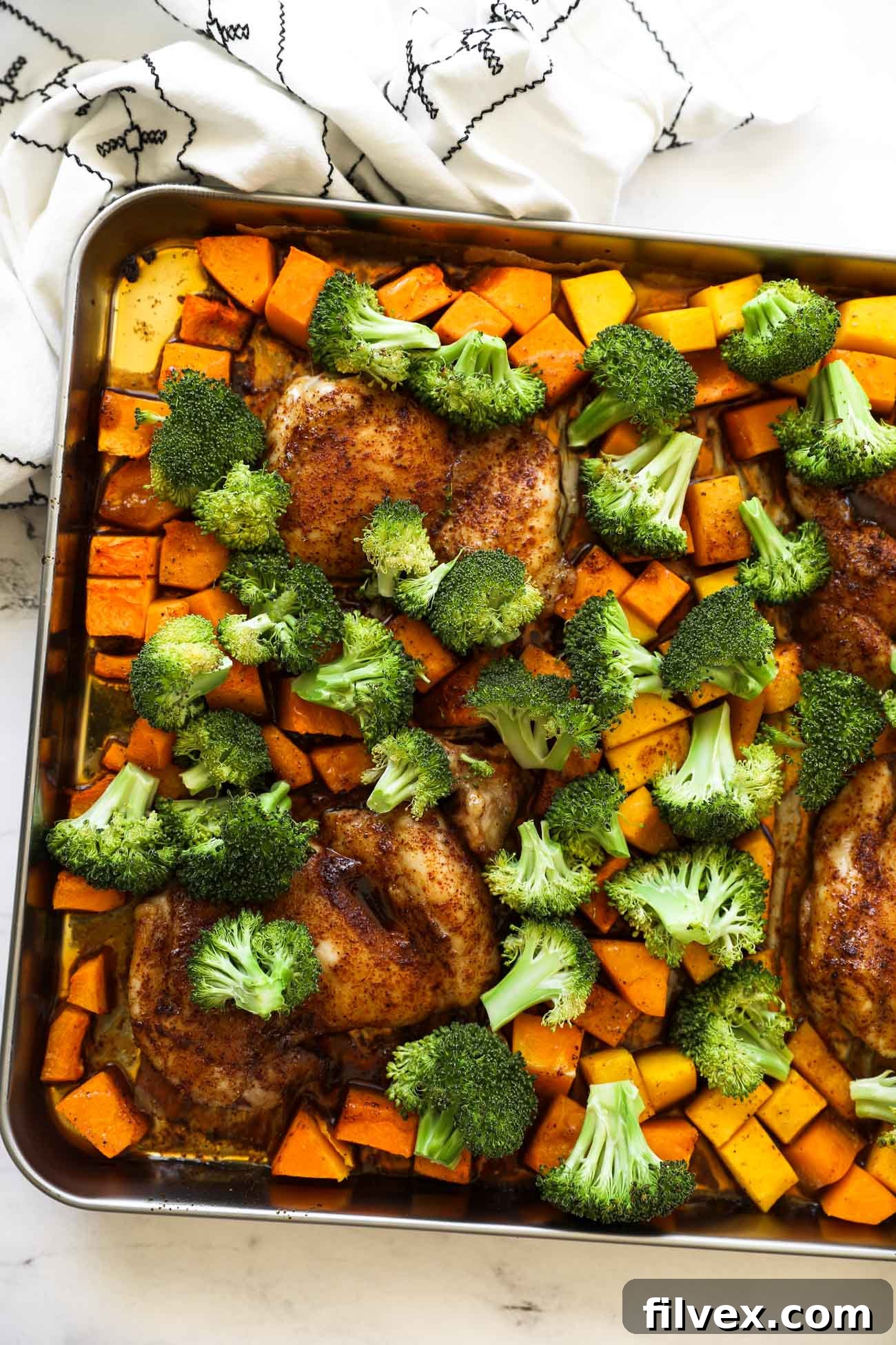 Golden brown chicken and vibrant green broccoli with roasted butternut squash on a baking sheet, fresh out of the oven.