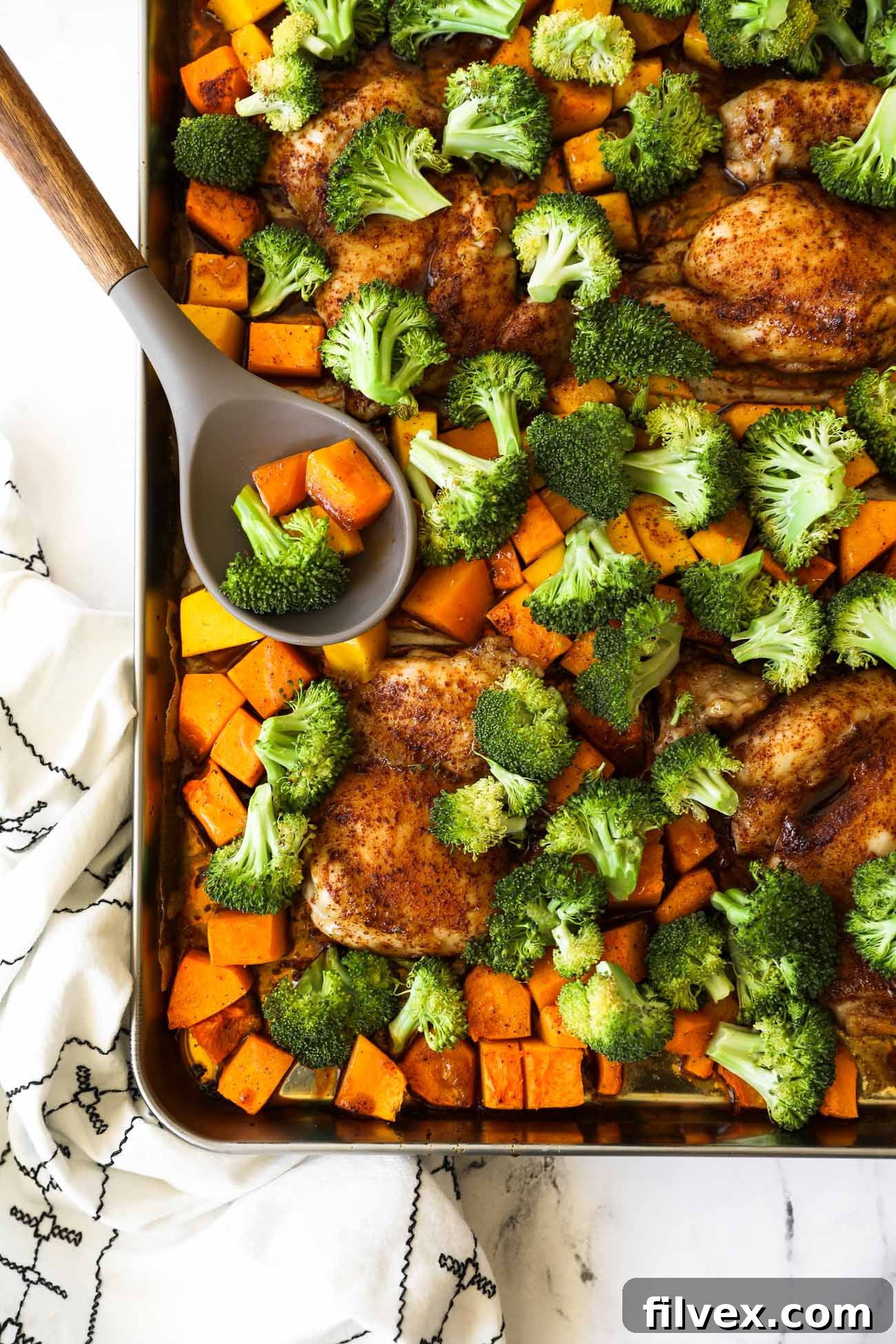 Close-up of raw chicken breasts and diced butternut squash arranged on a parchment-lined baking sheet, ready for the oven.