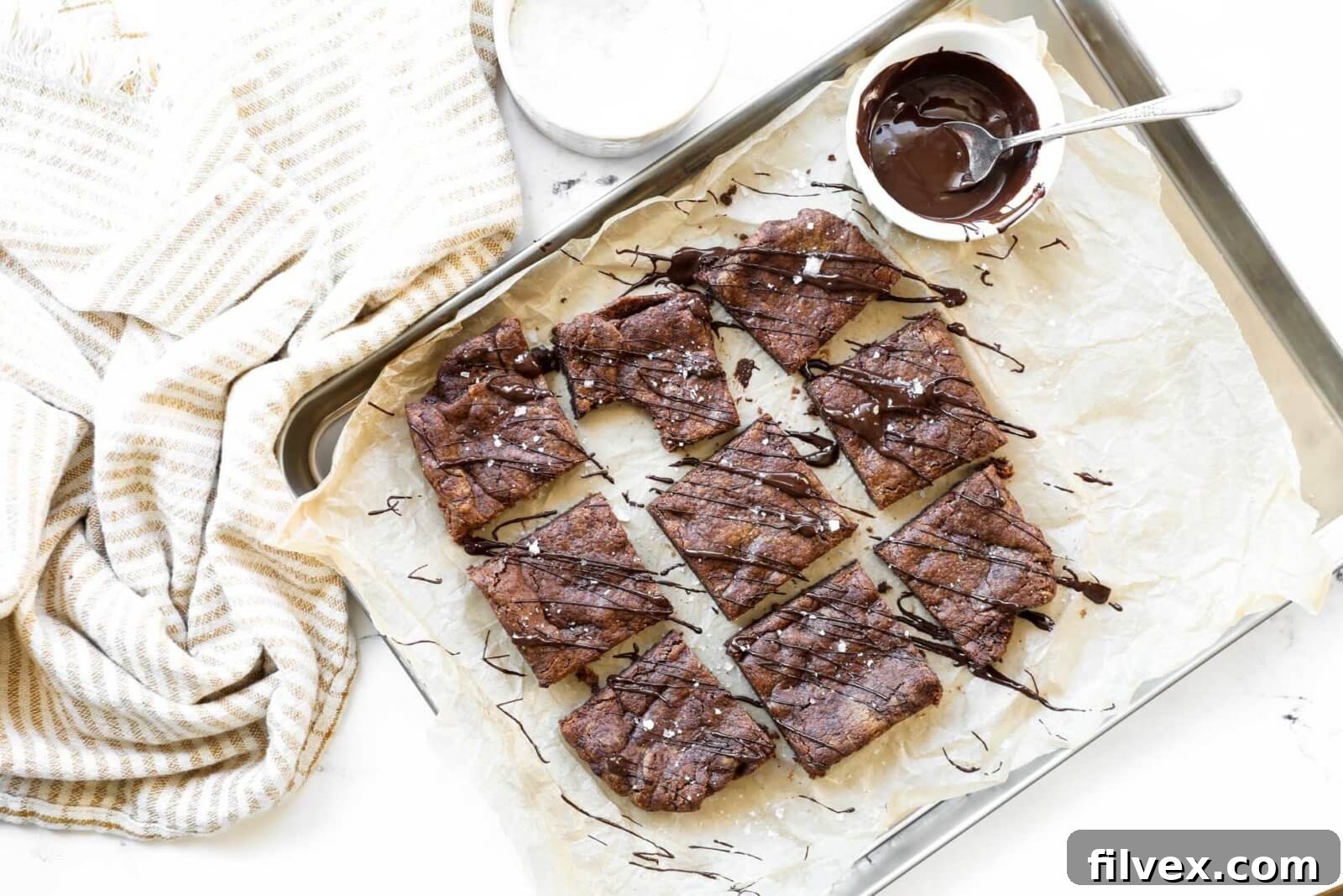 Horizontal overhead image of dairy free brownies sliced into squares on a sheet pan. Drizzled with melted chocolate and sprinkled with flaky sea salt. 