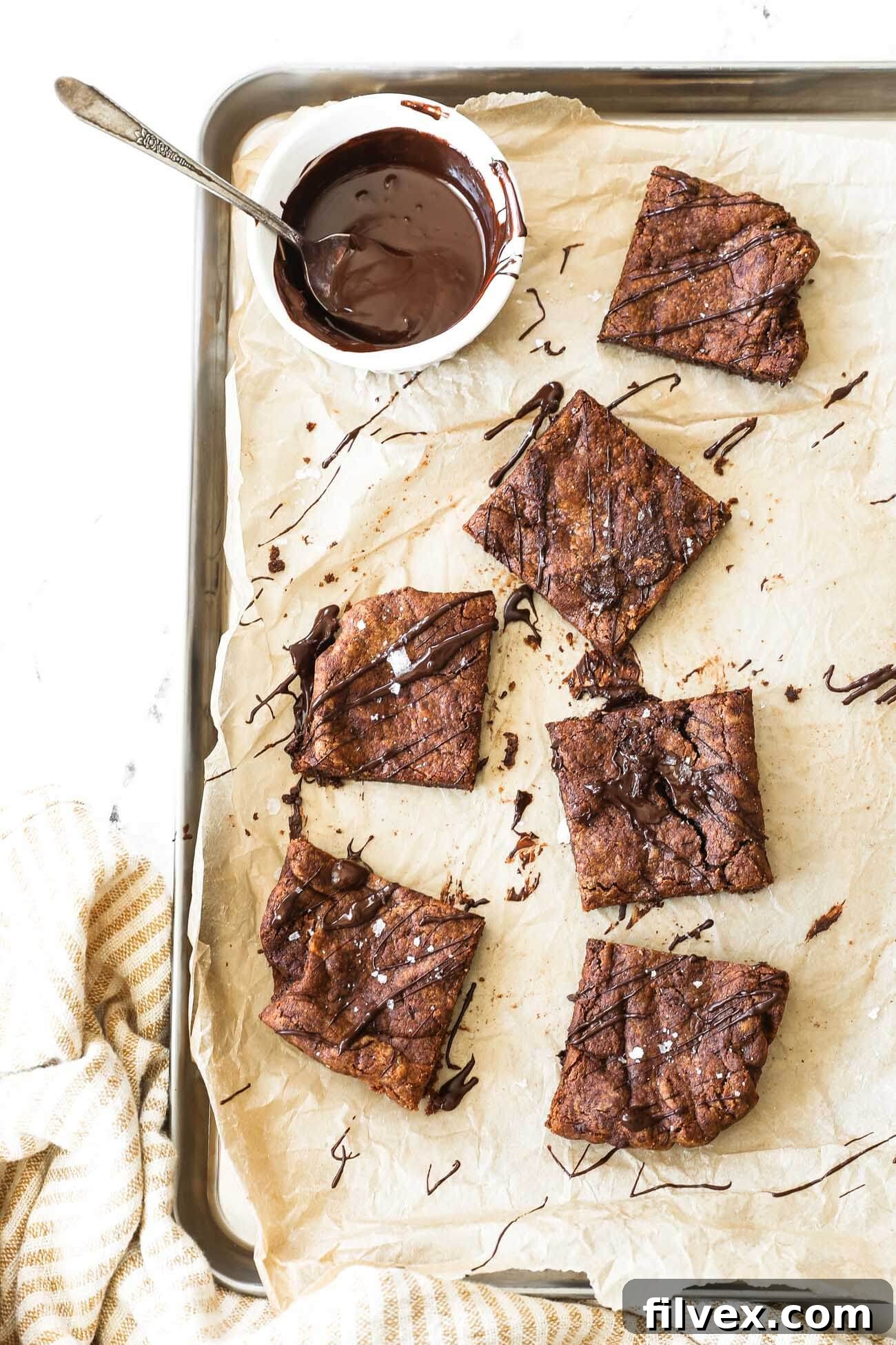 Close-up vertical image of dairy-free flourless brownies with a generous drizzle of melted chocolate and a sprinkle of flaky sea salt.