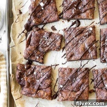 Vertical overhead image of flourless brownies sliced into squares and drizzled with melted chocolate on top. Also sprinkled with flaky sea salt.