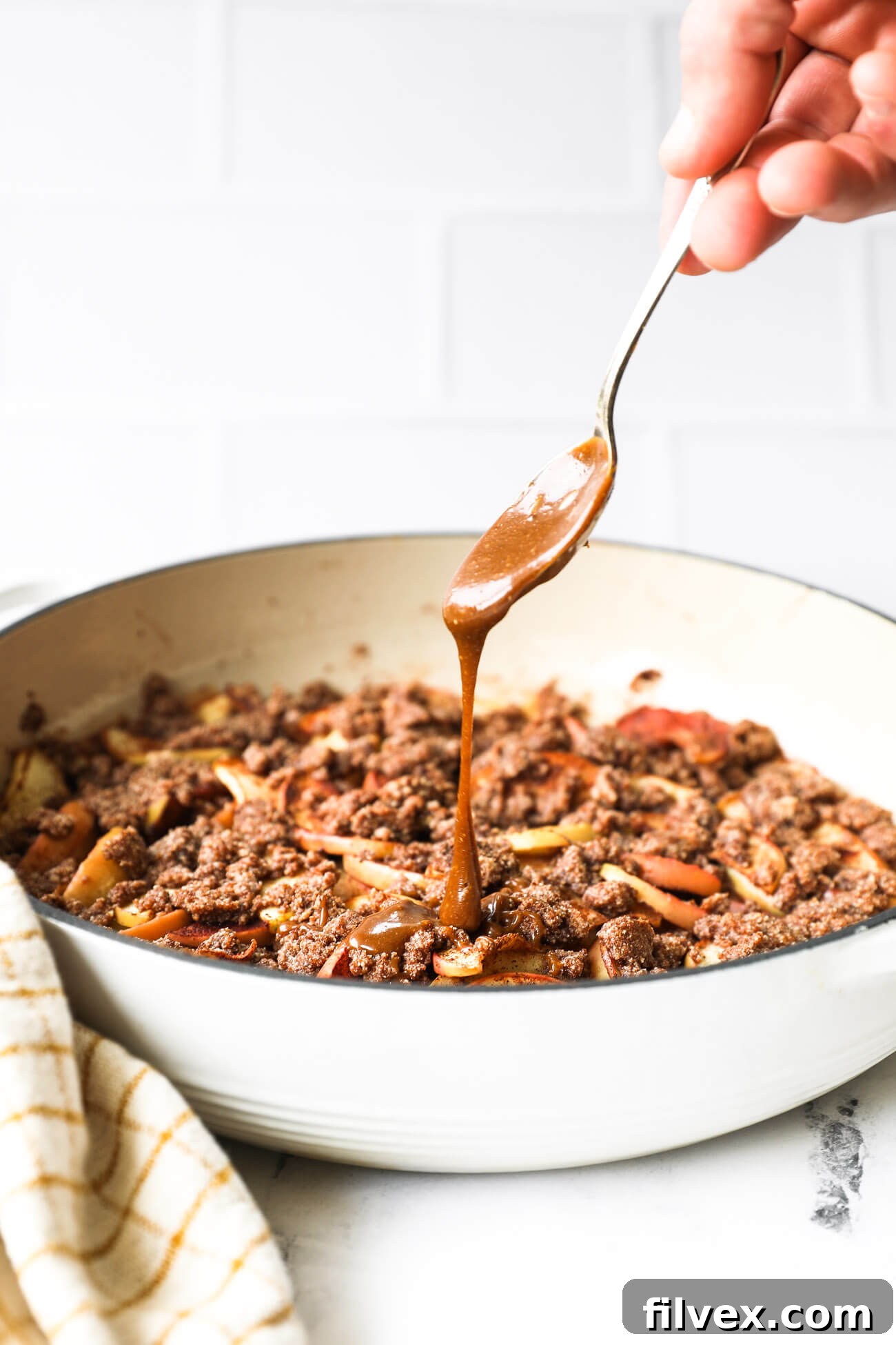 A beautifully presented slice of gluten-free vegan apple crumble, generously drizzled with salted caramel sauce, garnished with a sprig of mint, ready to be enjoyed.