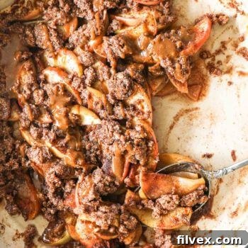 Close up image of apple crumble in skillet with some scooped out of the pan. Salted caramel sauce drizzled on top.