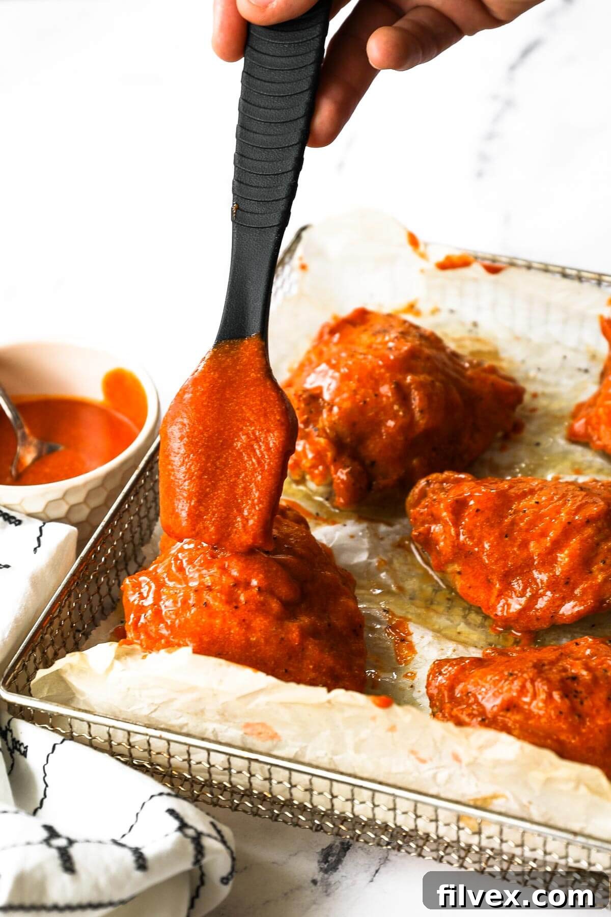 Cooked buffalo chicken thighs on a baking sheet with roasted vegetables