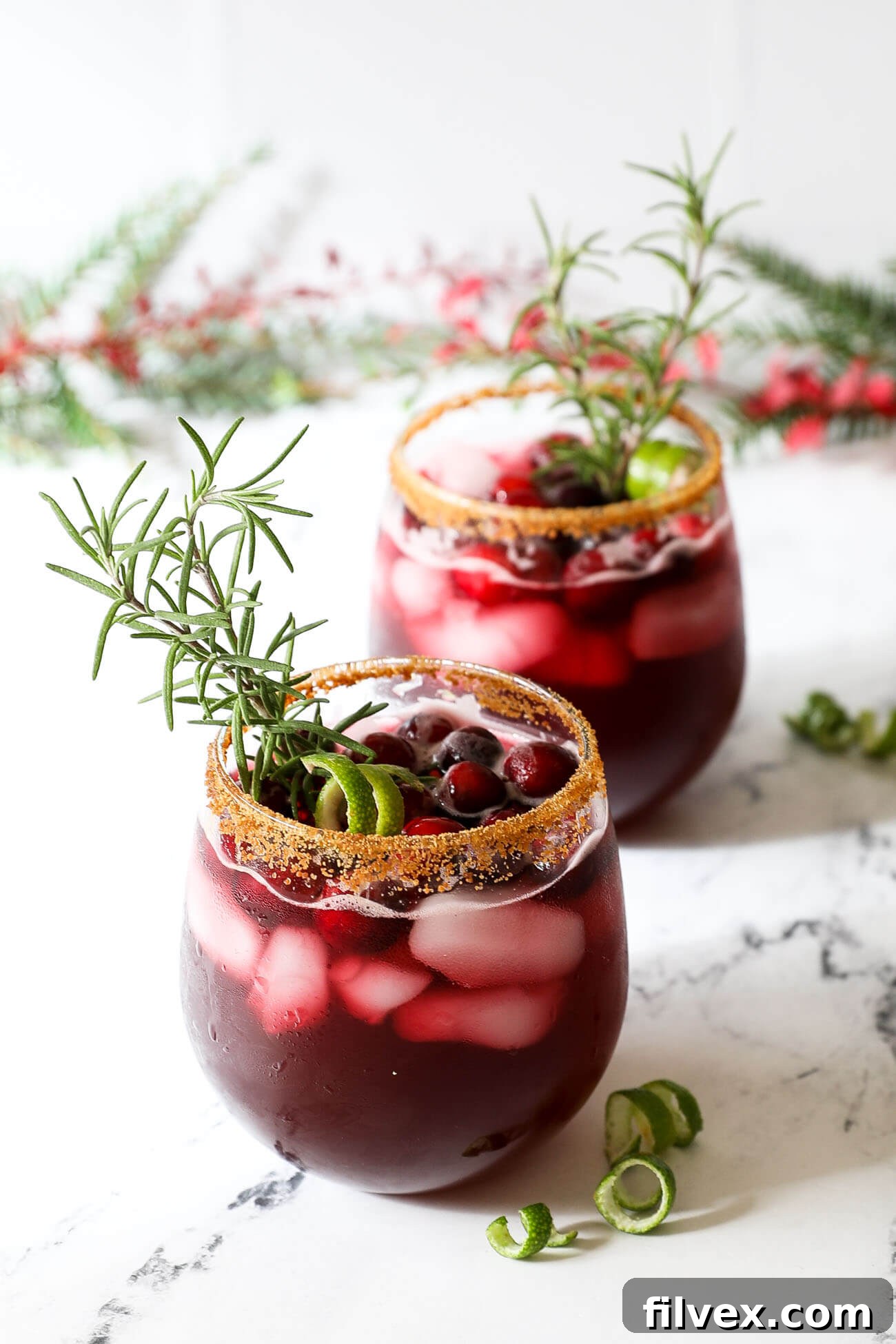 A vibrant red Christmas gin cocktail adorned with rosemary and cranberries, perfect for festive celebrations.