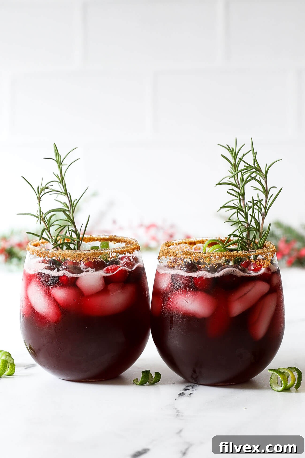 Two festive red gin cocktails, garnished with fresh cranberries and a sprig of rosemary, ready for a holiday party.
