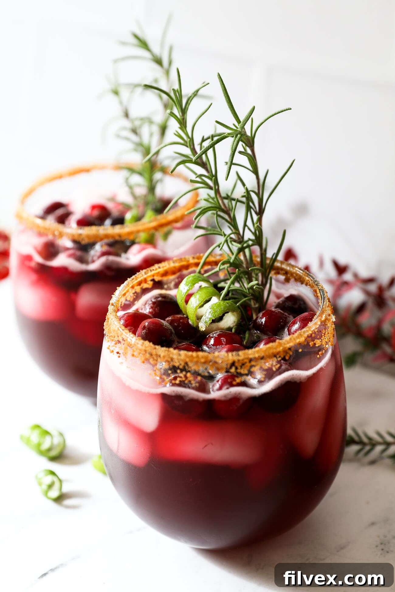 Four glasses of red Christmas cocktails, some garnished with lime and cranberries, set against a festive backdrop.
