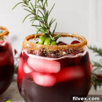 Close up straight on shot of red iced drink with brown sugar rim and rosemary sprig garnish