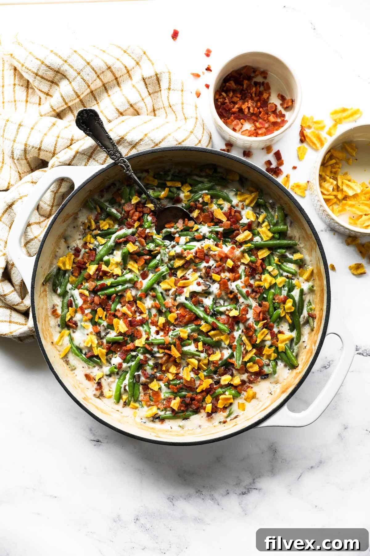 Overhead image of a skillet with green beans, a dairy free cream of mushroom sauce, crumbled bacon and plantain chips on top.