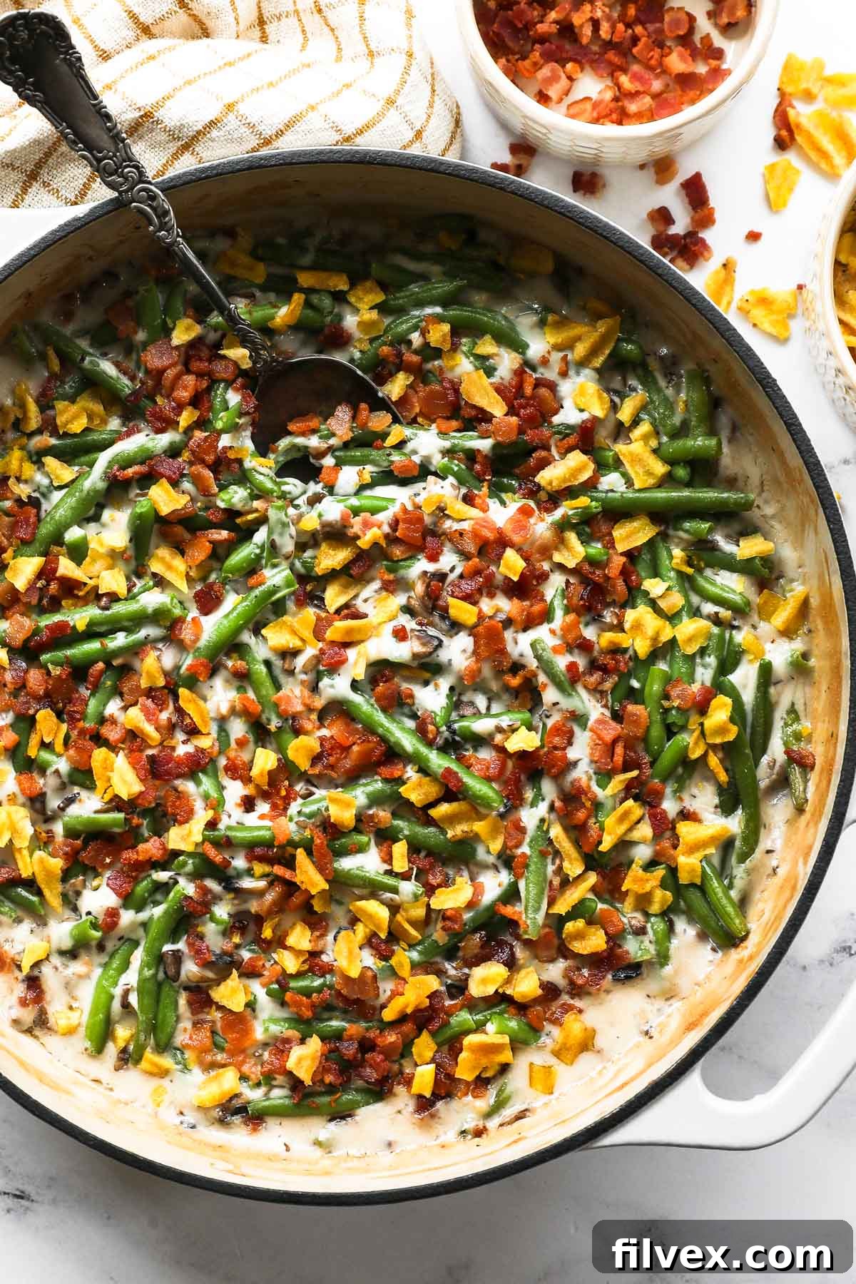Close up overhead image of a skillet with green beans, a dairy free cream of mushroom sauce, crumbled bacon and plantain chips on top.