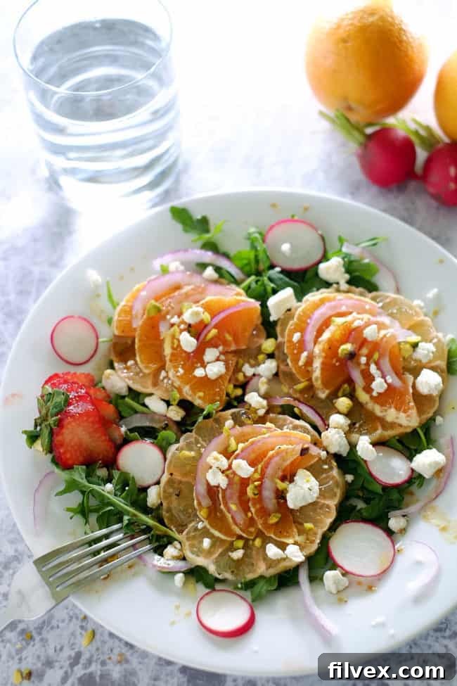 A close-up of the summer citrus salad featuring vibrant arugula, thinly sliced oranges, grapefruit, radishes, and crumbled goat cheese, topped with chopped pistachios. This healthy, gluten-free, and refined sugar-free recipe is a must-try.