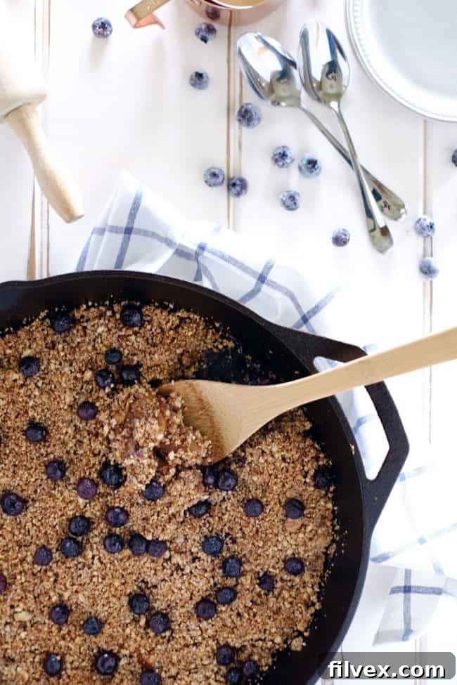 A close-up of a rustic paleo apple crisp, showcasing its savory-sweet flavors and crumbly texture, baked in a cast iron skillet. A gluten-free, dairy-free, vegan, and refined sugar-free dessert.