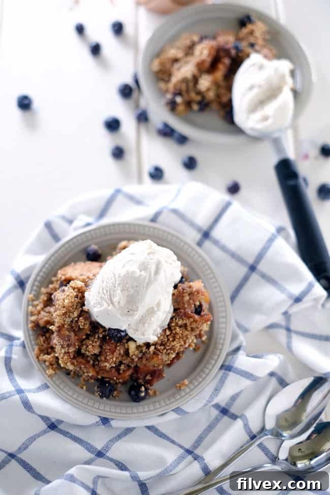 A generous serving of paleo apple crisp in a cast iron skillet, garnished with fresh blueberries. This gluten-free, dairy-free, vegan, and refined sugar-free dessert is perfect for sharing.