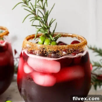 Close up straight on shot of red iced drink with brown sugar rim and rosemary sprig garnish