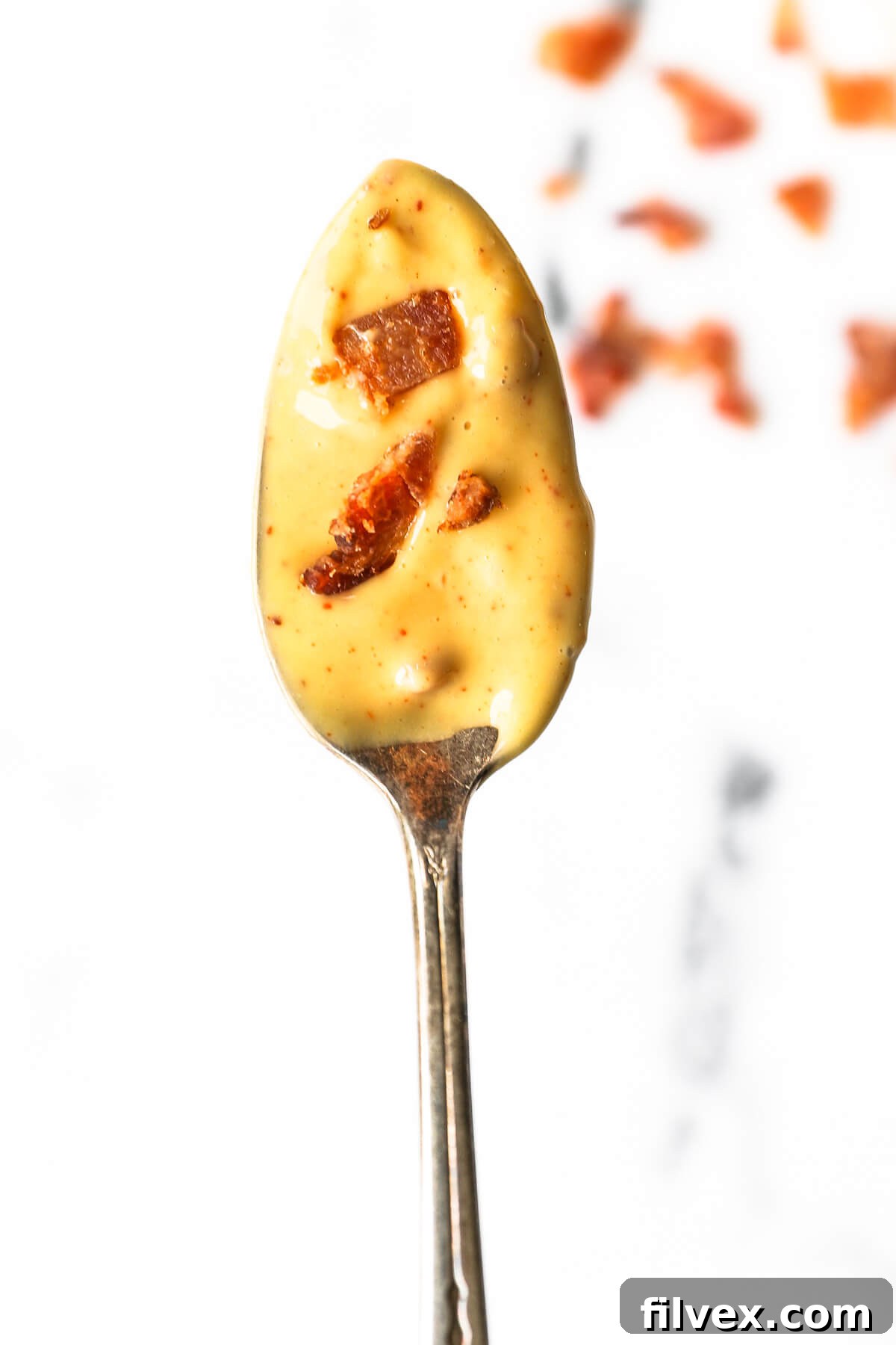 Side view of a bowl of bacon aioli with a spoon, ready to be served