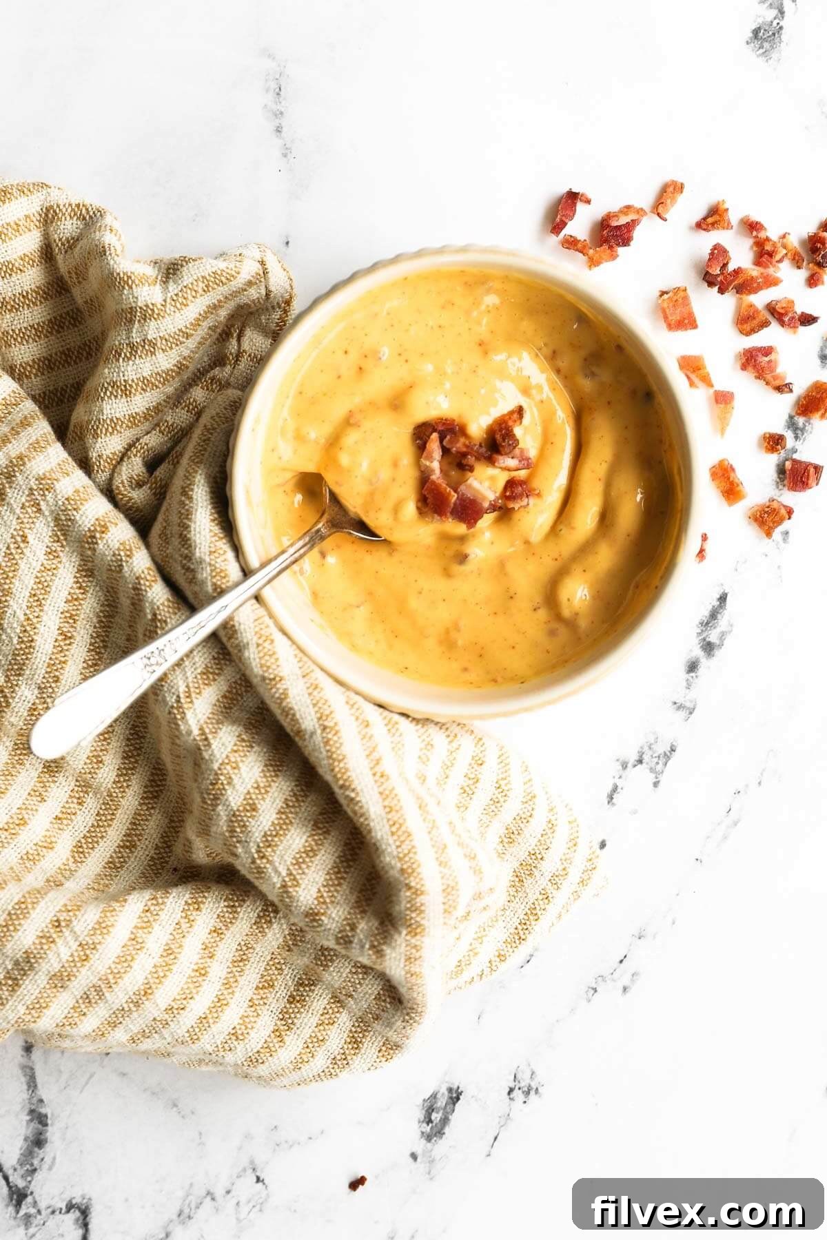 Overhead shot of bacon aioli in a ramekin with spoon and bacon pieces on the top and side