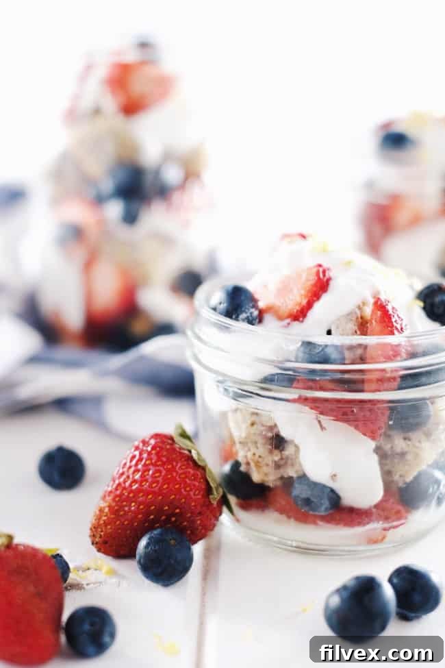 Layered Berry Lemon Shortcake in individual mason jars, topped with fresh blueberries, strawberries, and coconut whipped cream. Paleo friendly.