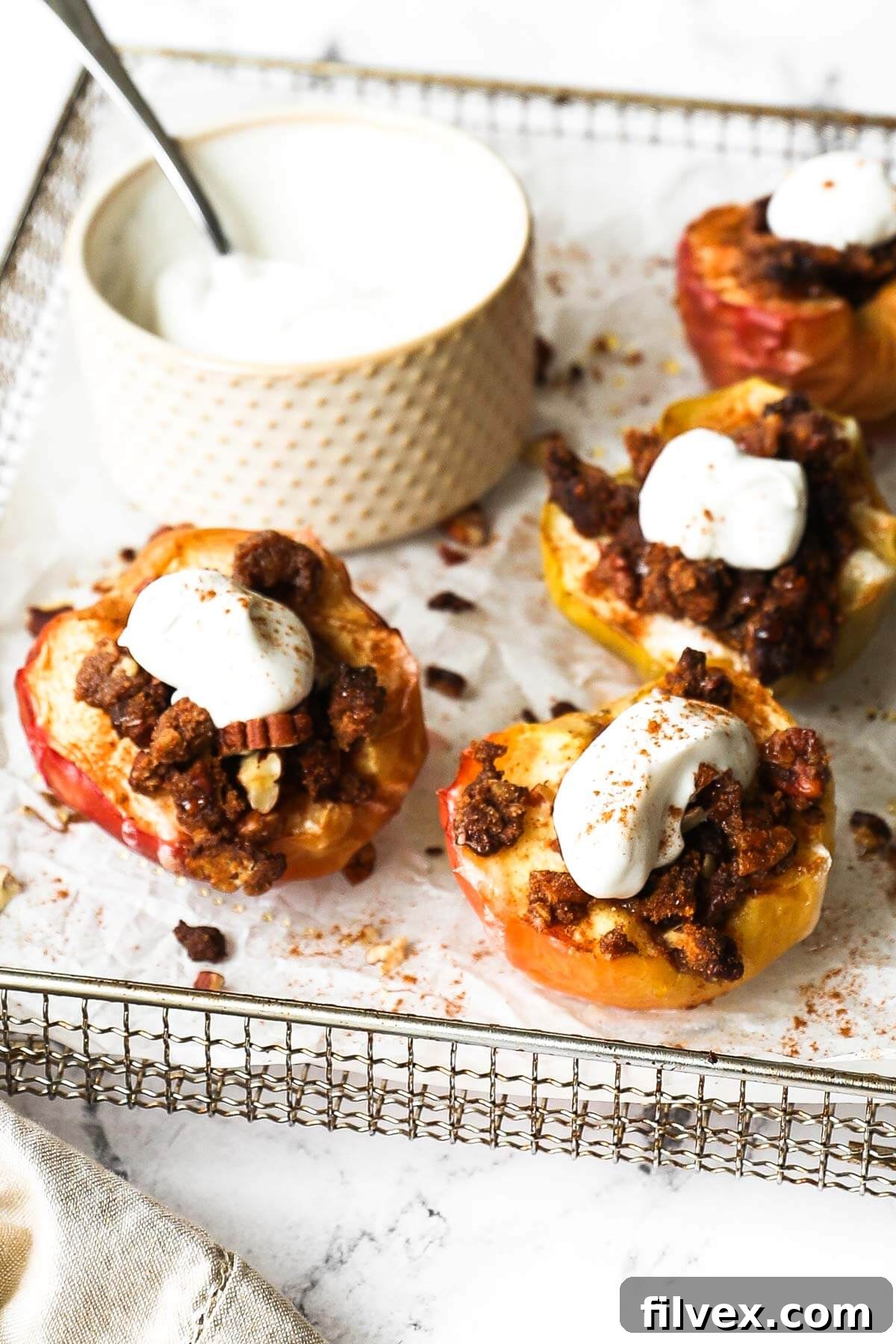 Angled image of air fryer cinnamon baked apples in the air fryer basket topped with a crumble topping and whipped coconut cream.