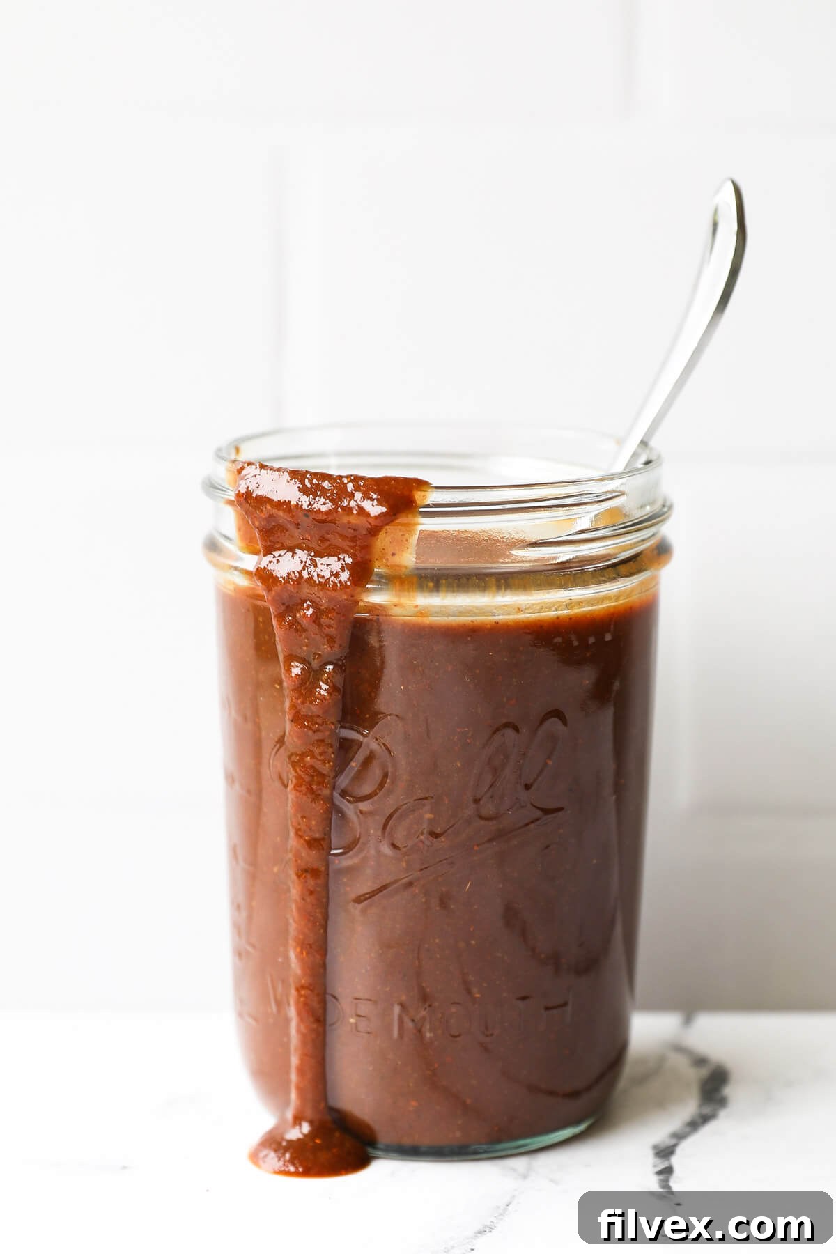 A bottle of homemade Whole30 BBQ sauce with fresh ingredients like tomatoes and spices