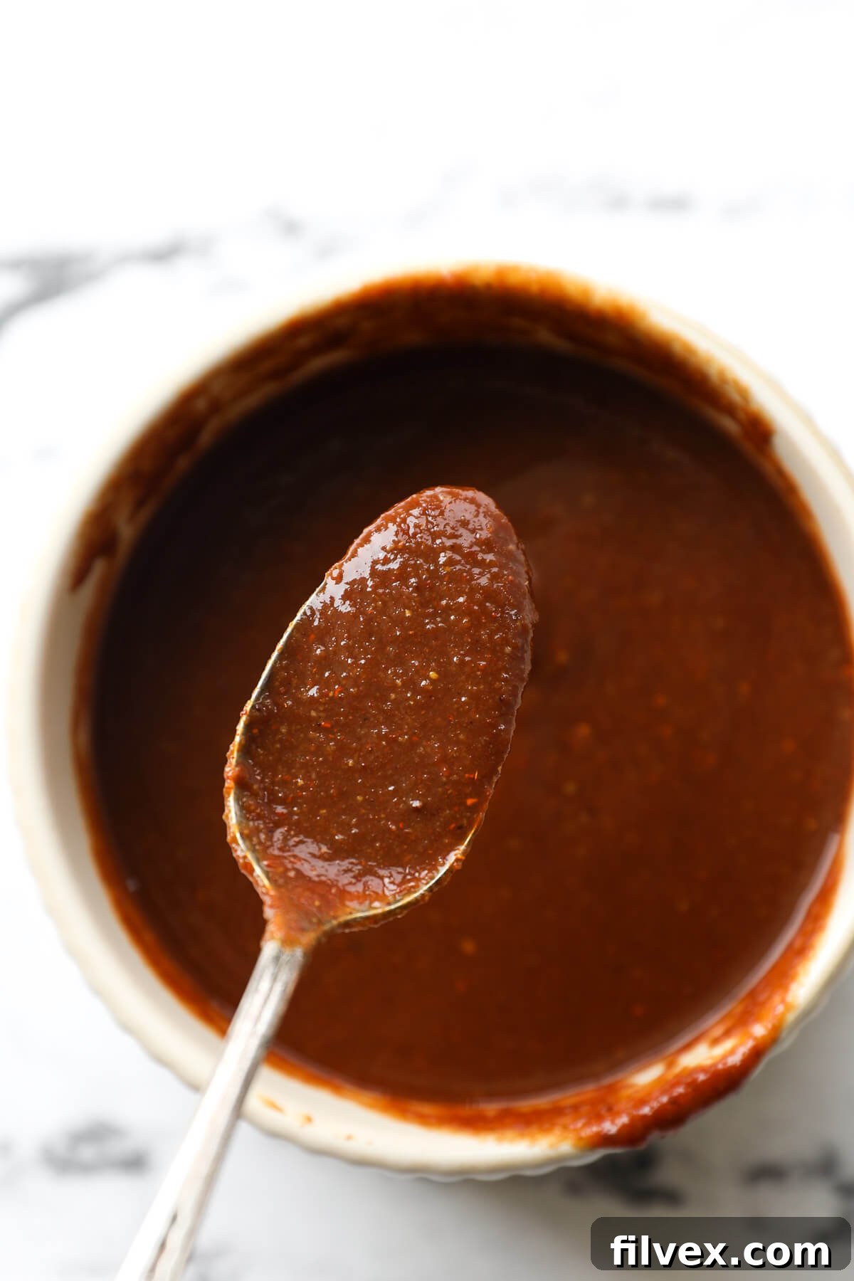 A spoon scooping homemade Whole30 BBQ sauce from a ramekin