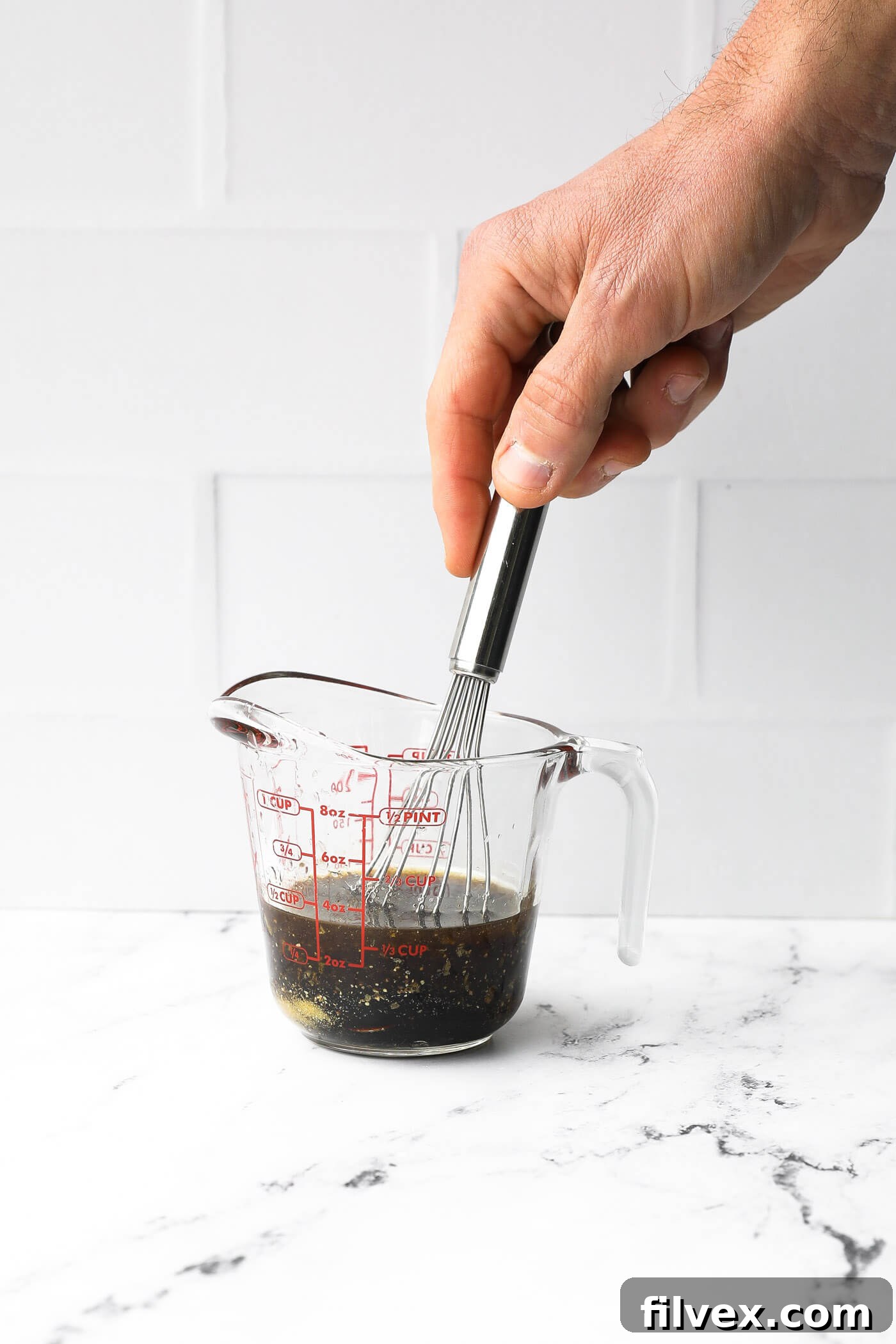 A small bowl containing the liquid marinade ingredients, with a whisk nearby, illustrating the mixing process.