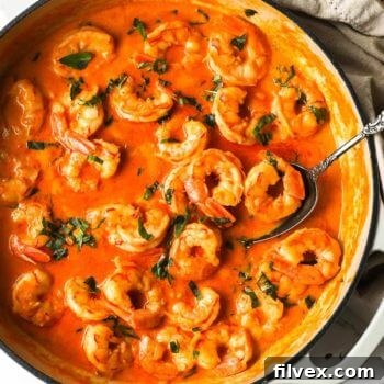 Overhead image of cooked creamy coconut shrimp in a pan with spoon and basil garnish