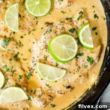 Coconut lime chicken with a creamy light orange sauce in a cast iron skillet with lime wedges and chopped cilantro on top