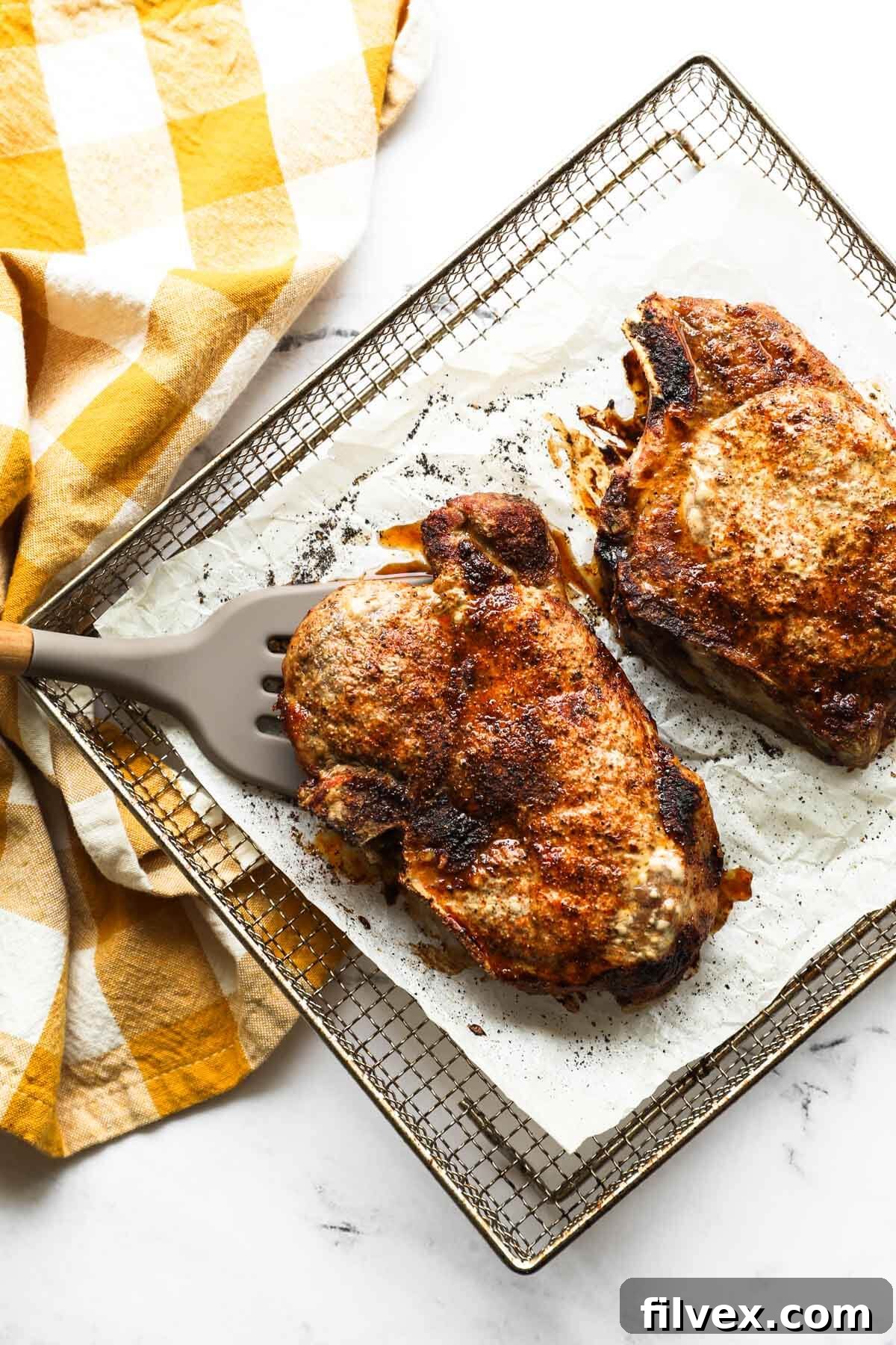 Two perfectly cooked bone-in pork chops with a golden crust in an air fryer basket, garnished with fresh herbs.