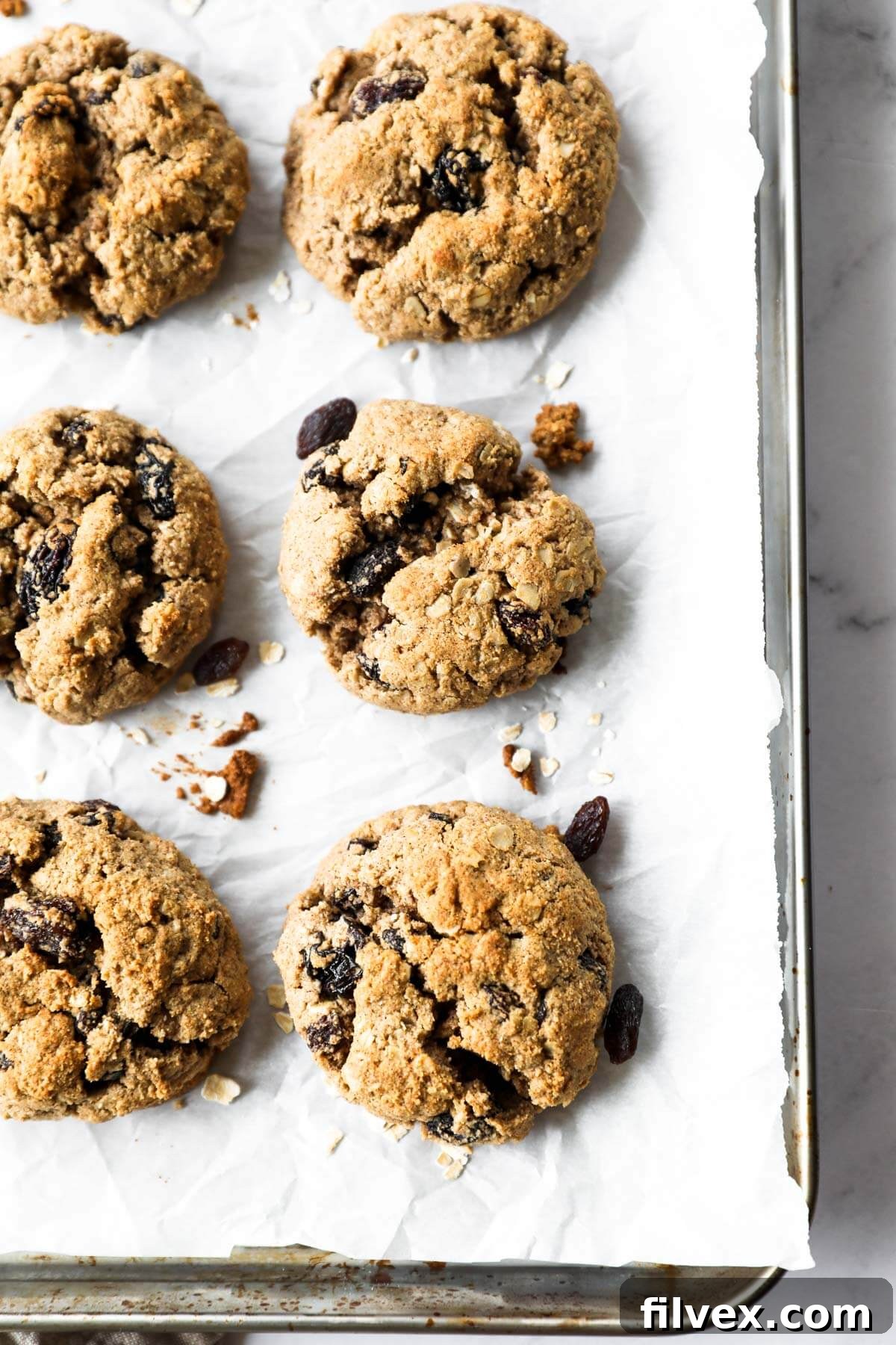 Overhead close up image of six vegan oatmeal raisin cookies on a baking sheet.