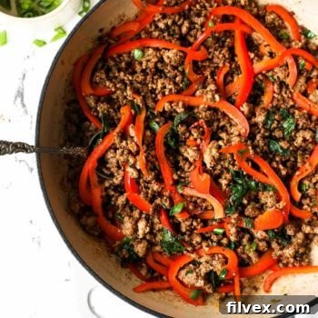 Thai basil pork stir fry in a pan with sliced red bell peppers and spoon sticking out, ready to be served