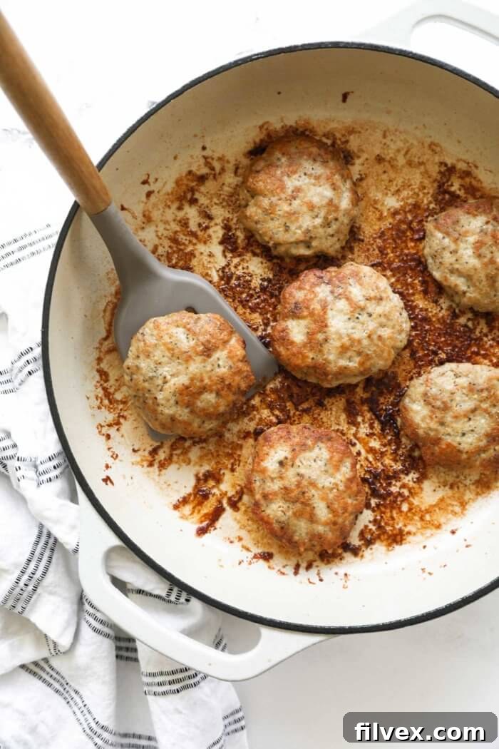 Overhead image of a cast iron skillet with chicken sausage patties in it. A spatula lifting one patty out of the pan.