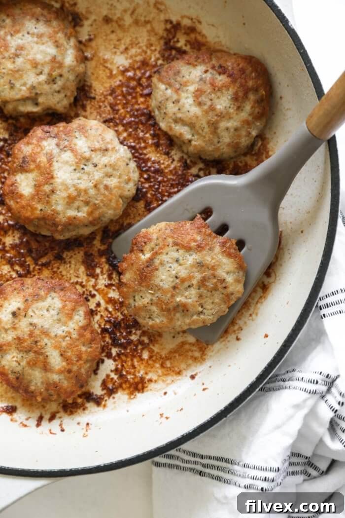 Close up overhead image of skillet with one sausage patty being lifted by a spatula.