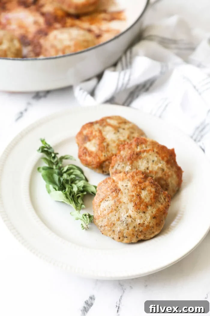 Angled image of three chicken sausage patties on a plate with fresh oregano on the side.